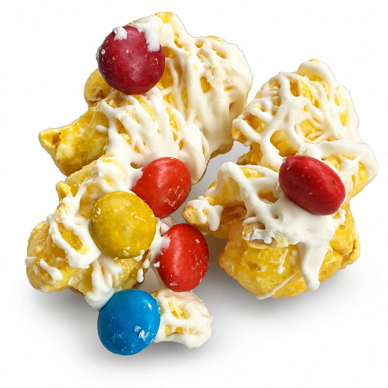 Four yellow popcorn clusters topped with white chocolate drizzle and colorful candy-coated beads in red, yellow, blue, and red, arranged on a white background.